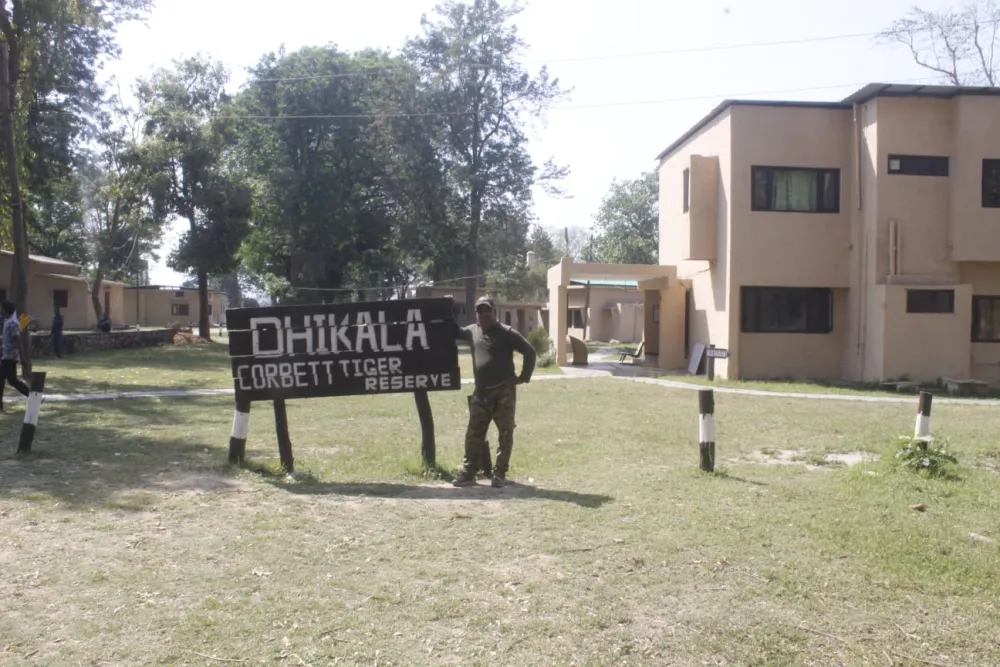 Forest guide beside the Dhikala signboard with rest house buildings in Corbett Tiger Reserve